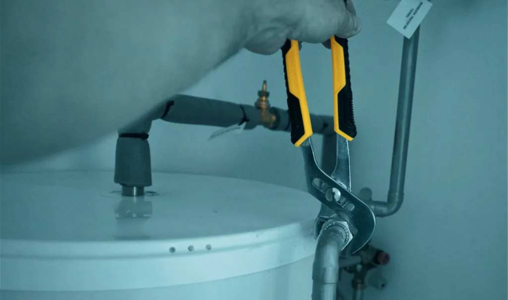 Loodgieter met een waterpomptang aan de leidingen van een boiler